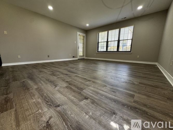 A spacious room with wooden flooring and a window with blinds.