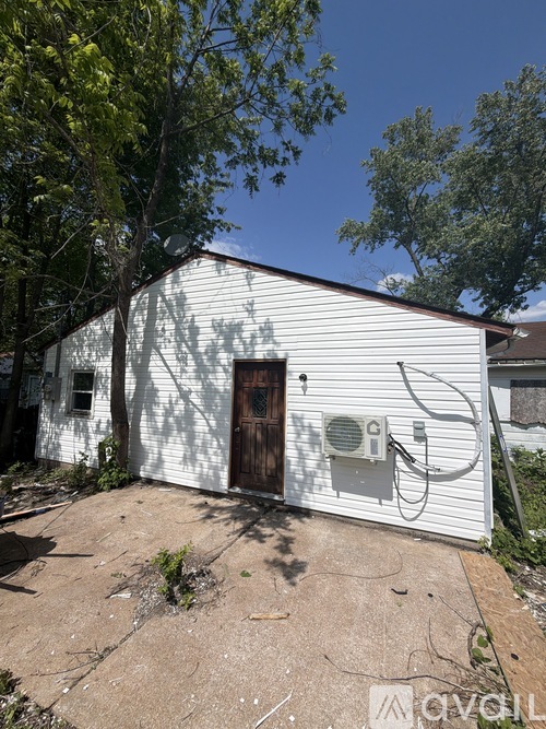 A white building with a brown door and a window is surrounded by trees.