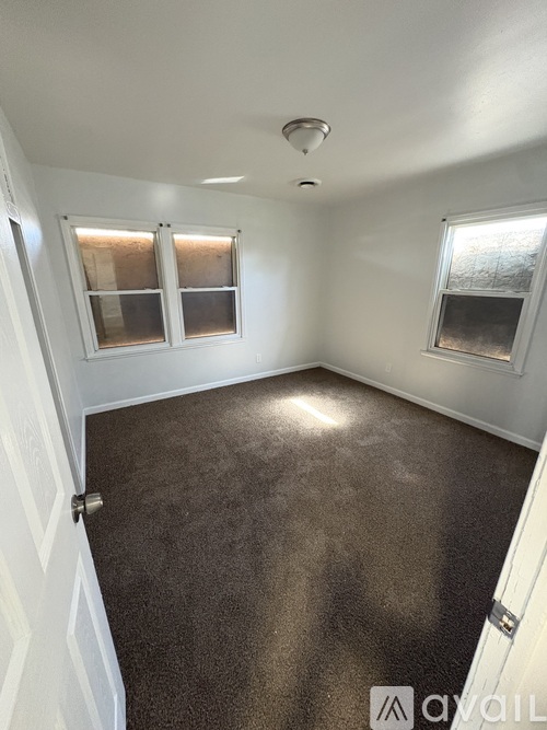 A room with brown carpet and two windows.