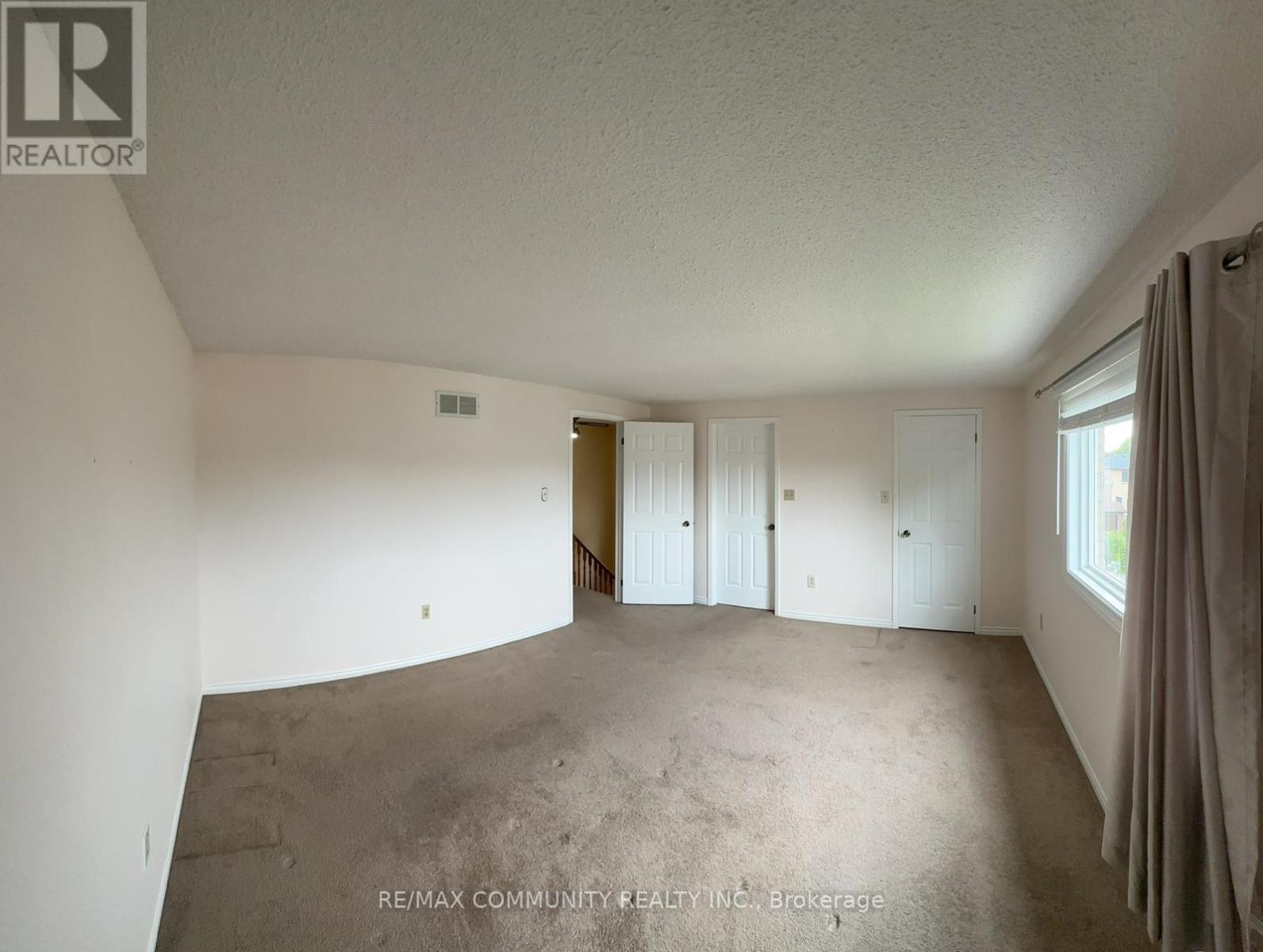 A spacious room with a carpeted floor and a window with curtains.