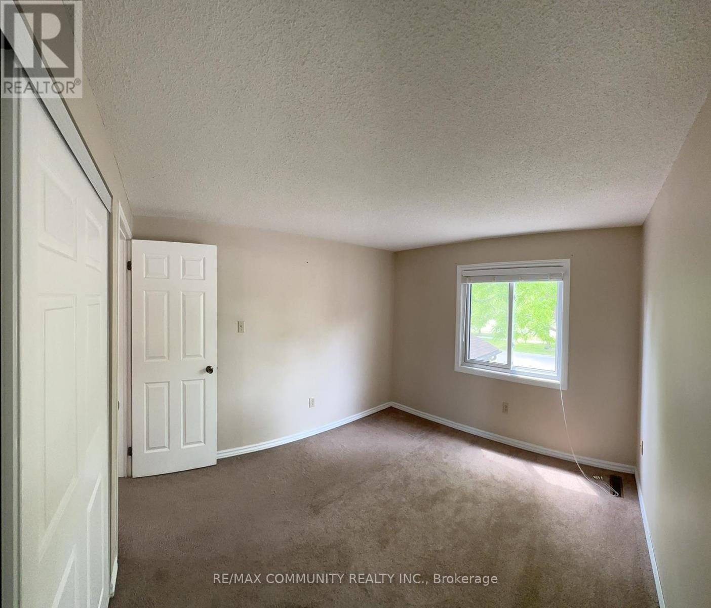 A room with a white door and a window with a view of trees outside.