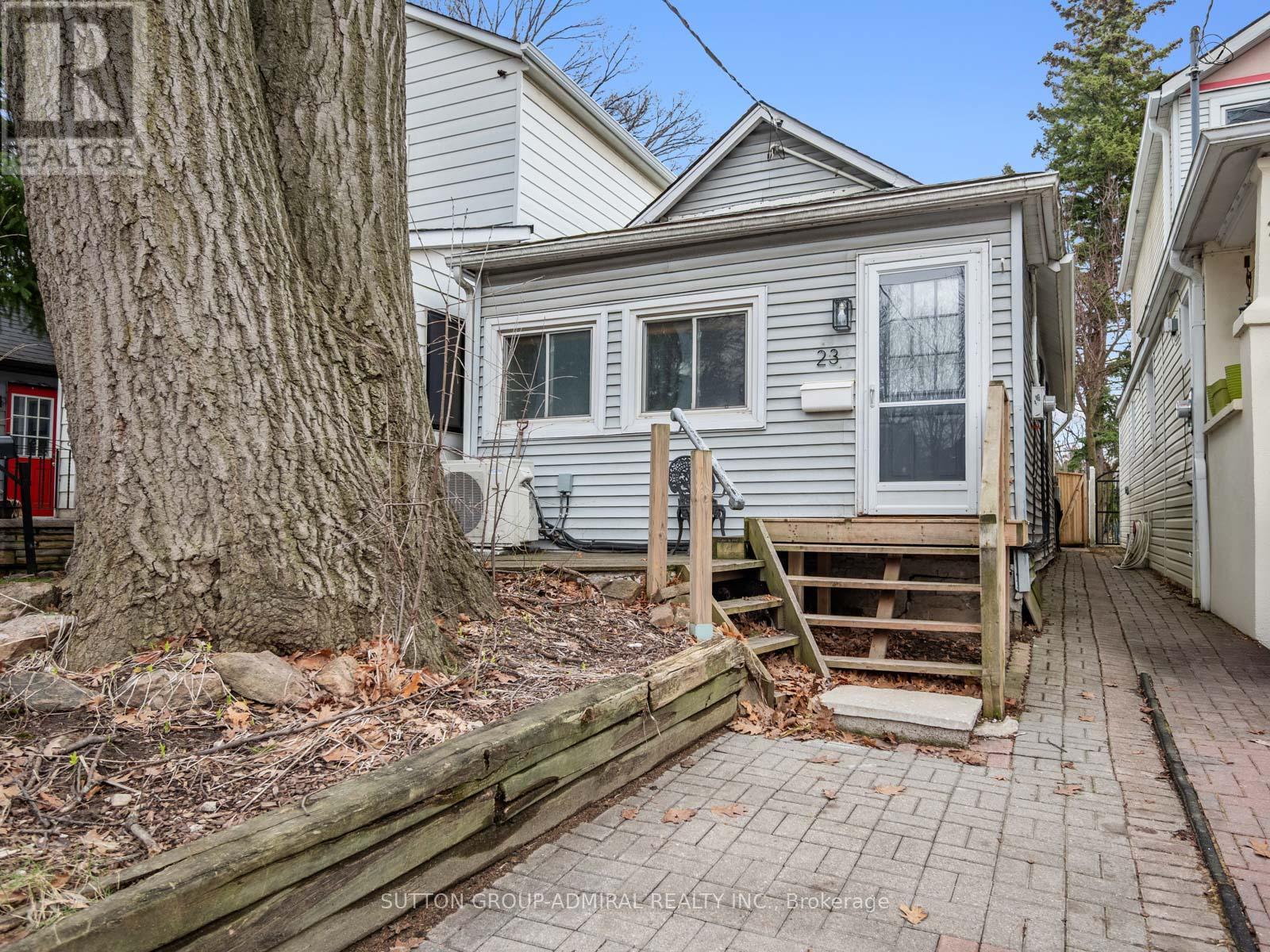 A house with a grey siding and a white door is surrounded by a wooden fence and a tree.