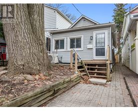 A house with a grey siding and a white door is surrounded by a wooden fence and a tree.