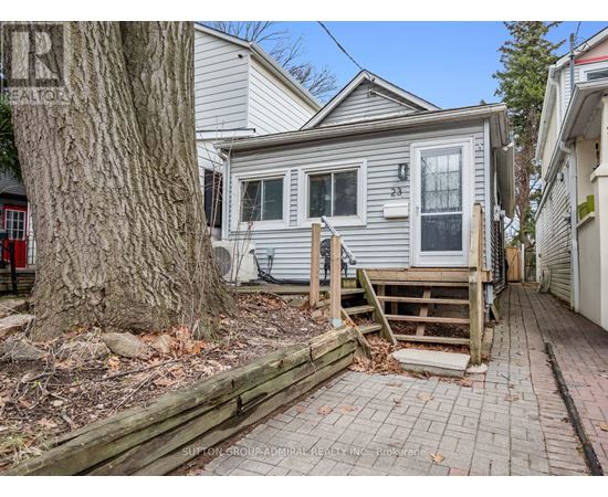 A house with a grey siding and a white door is surrounded by a wooden fence and a tree.