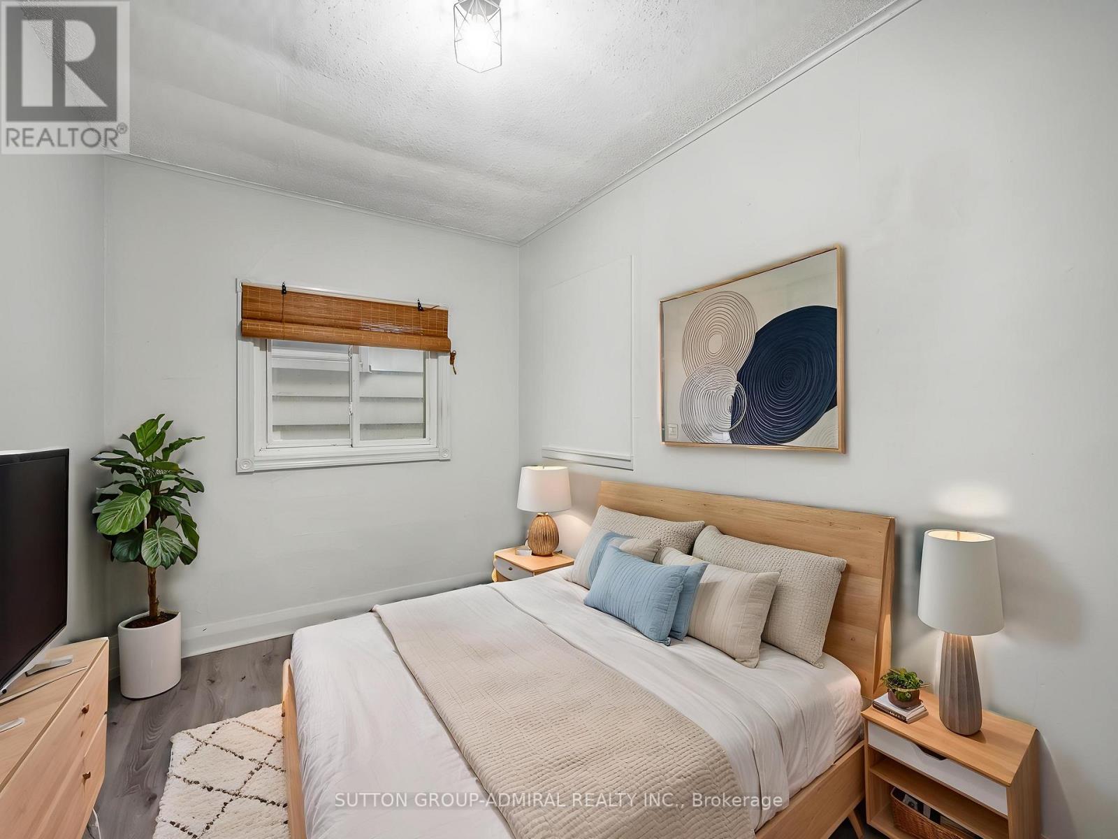 A bedroom with a large bed, a potted plant, and a painting on the wall.