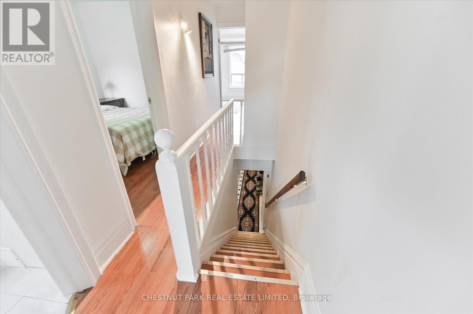 A staircase with a wooden floor and white railings leads to a bedroom.