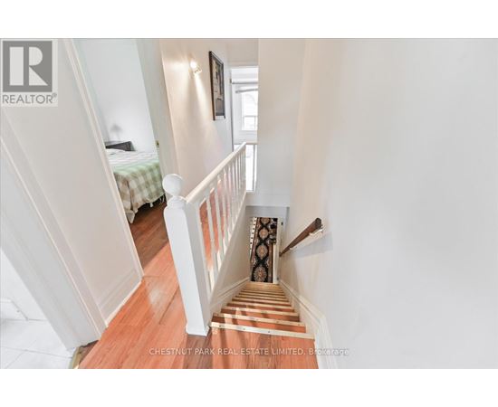 A staircase with a wooden floor and white railings leads to a bedroom.