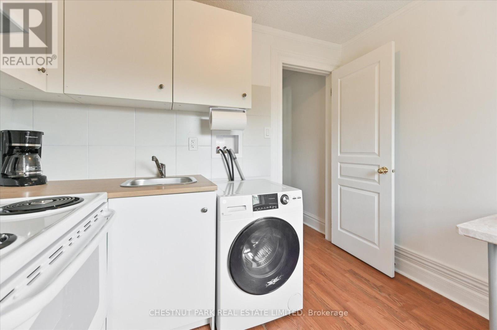 A white washing machine is in a kitchen with white cabinets.