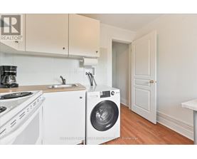 A white washing machine is in a kitchen with white cabinets.