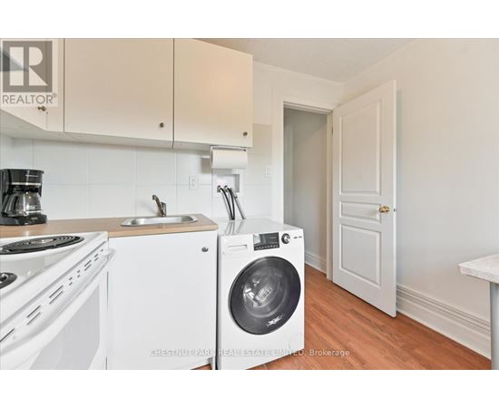 A white washing machine is in a kitchen with white cabinets.