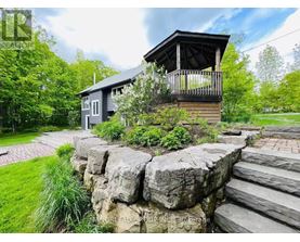 A house with a balcony is surrounded by greenery and a stone wall.