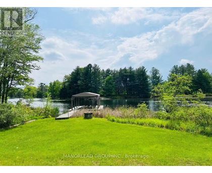 A gazebo sits on a grassy area by a lake.
