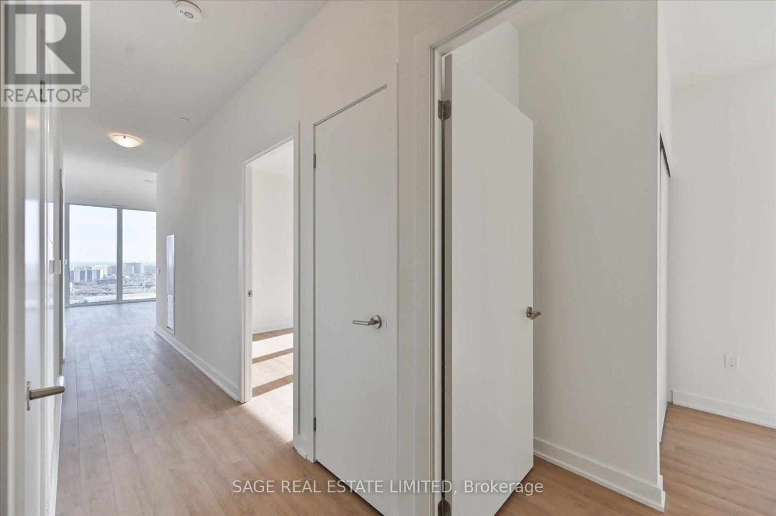A real estate listing image of a bedroom with white doors and a wooden floor.
