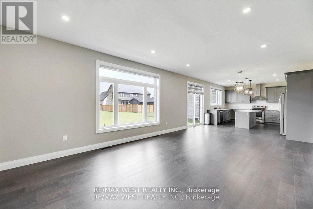 A spacious living room with a large window and a kitchen area in the background.