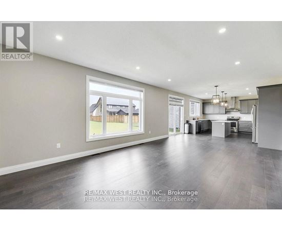 A spacious living room with a large window and a kitchen area in the background.