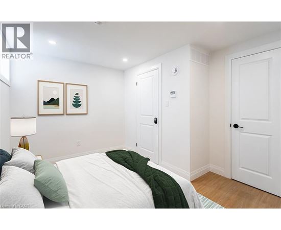 A bedroom with a bed, two pictures on the wall, and a lamp on the side table.