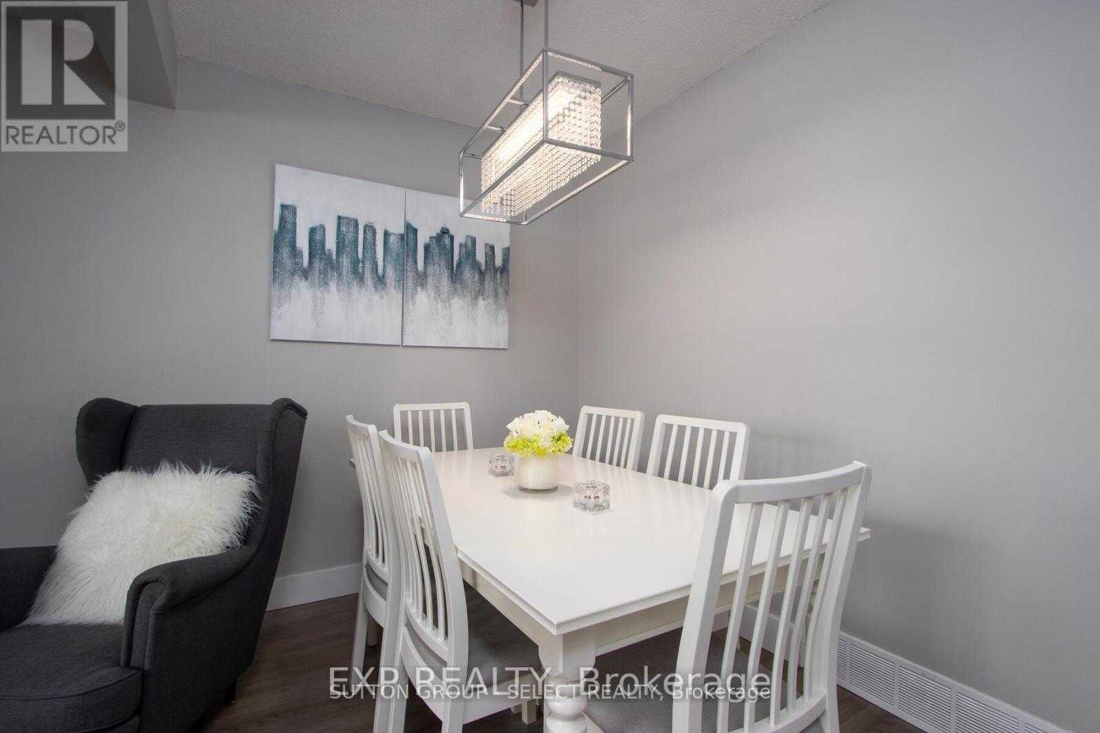 A dining room with a white table and chairs, a grey armchair, and a painting on the wall.
