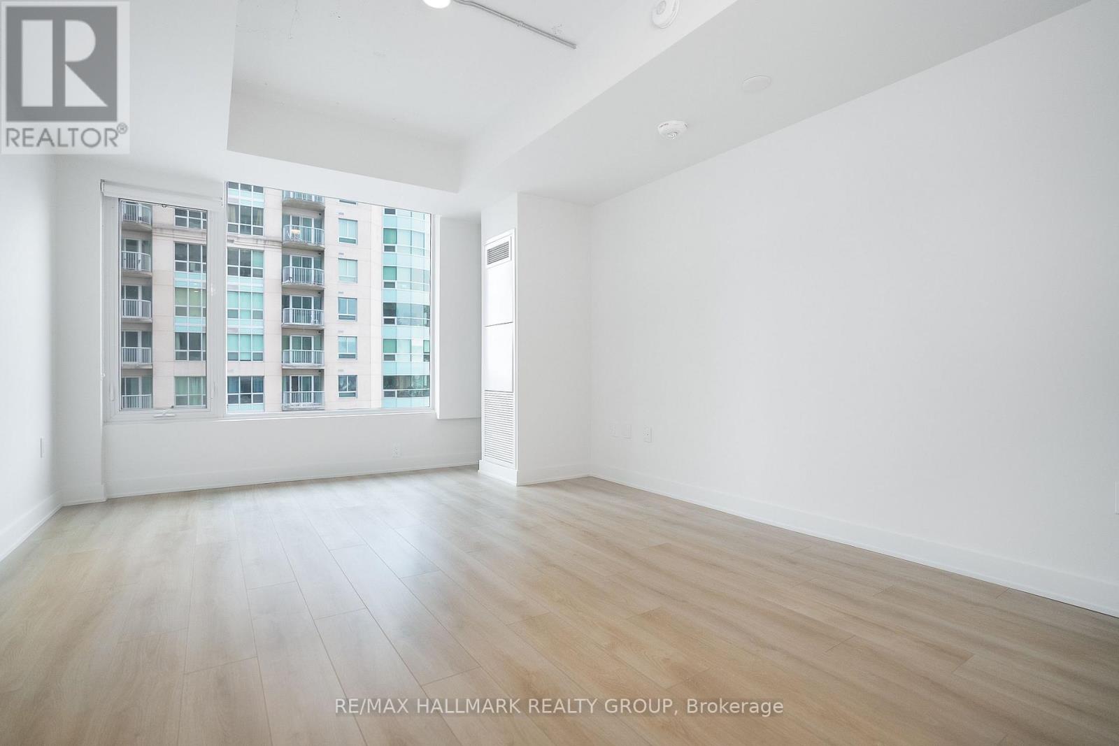 A spacious room with a large window and wooden flooring.