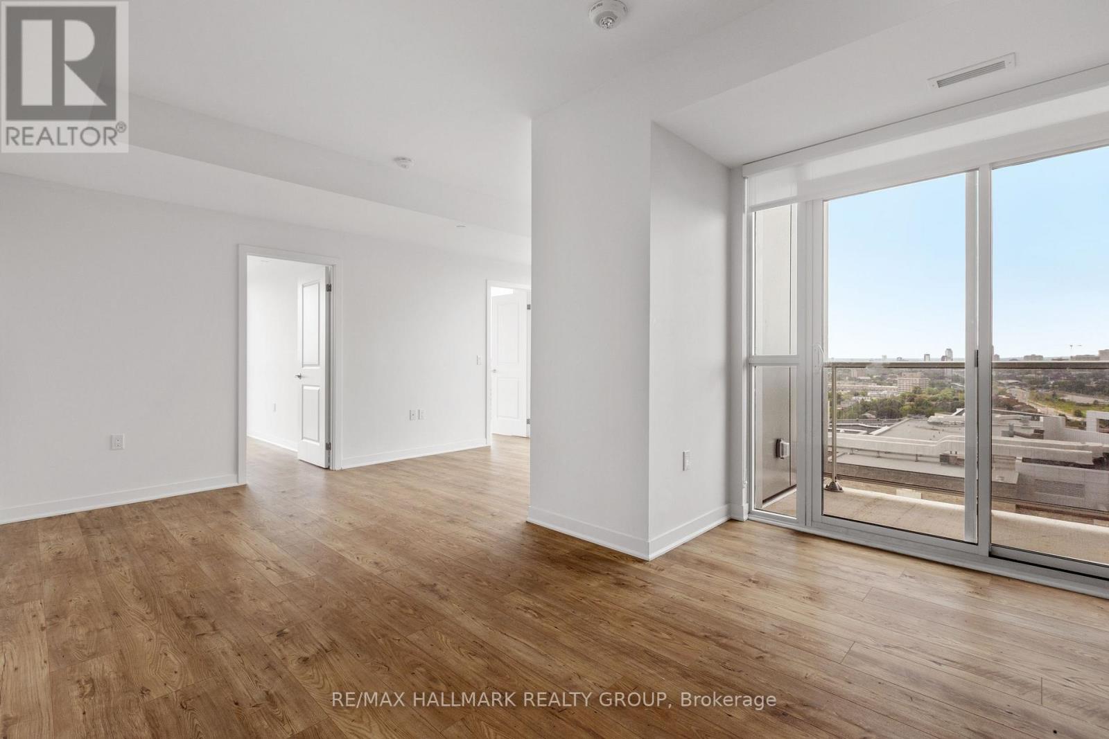 A spacious room with wooden floors and large windows overlooking a parking lot.