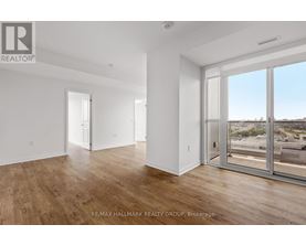 A spacious room with wooden floors and large windows overlooking a parking lot.