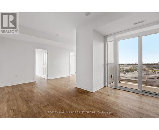 A spacious room with wooden floors and large windows overlooking a parking lot.
