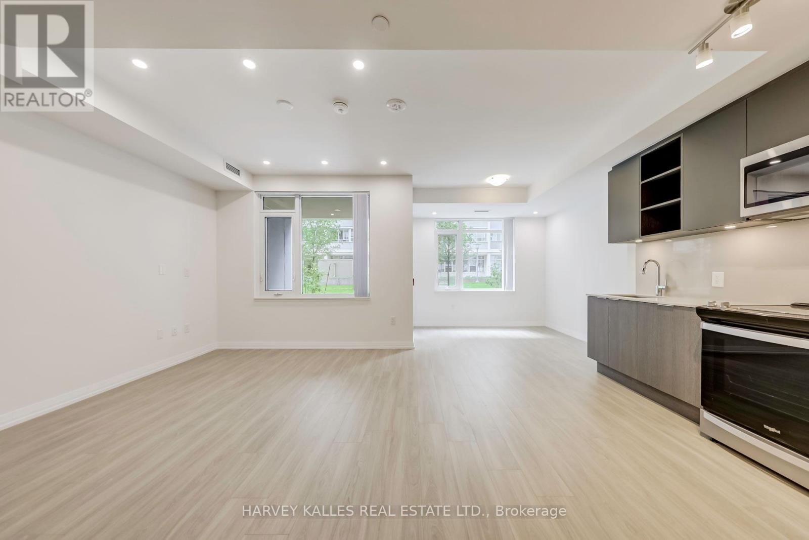 A spacious, well-lit room with wooden flooring and modern appliances in a real estate listing.