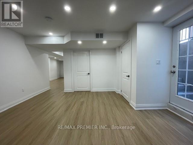 A spacious room with wooden flooring and white walls, with a door on the right side.