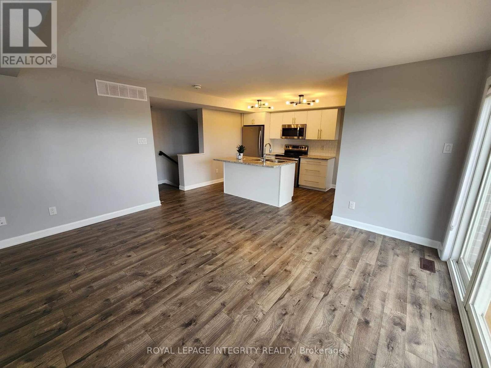 A spacious room with wooden flooring and a kitchen area in the background.