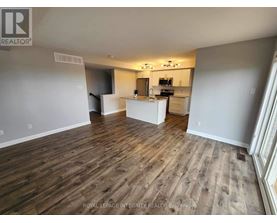 A spacious room with wooden flooring and a kitchen area in the background.