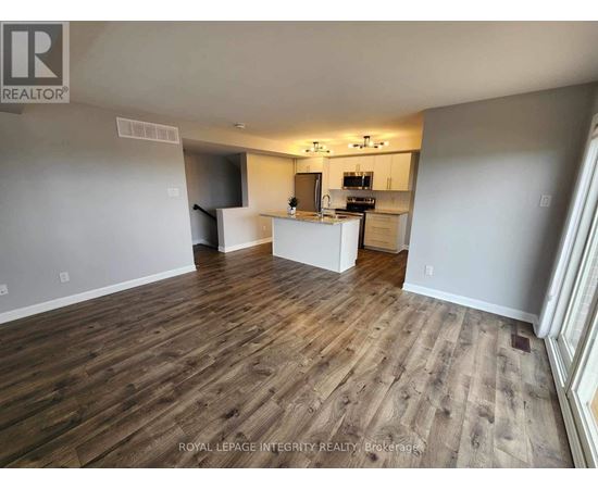 A spacious room with wooden flooring and a kitchen area in the background.