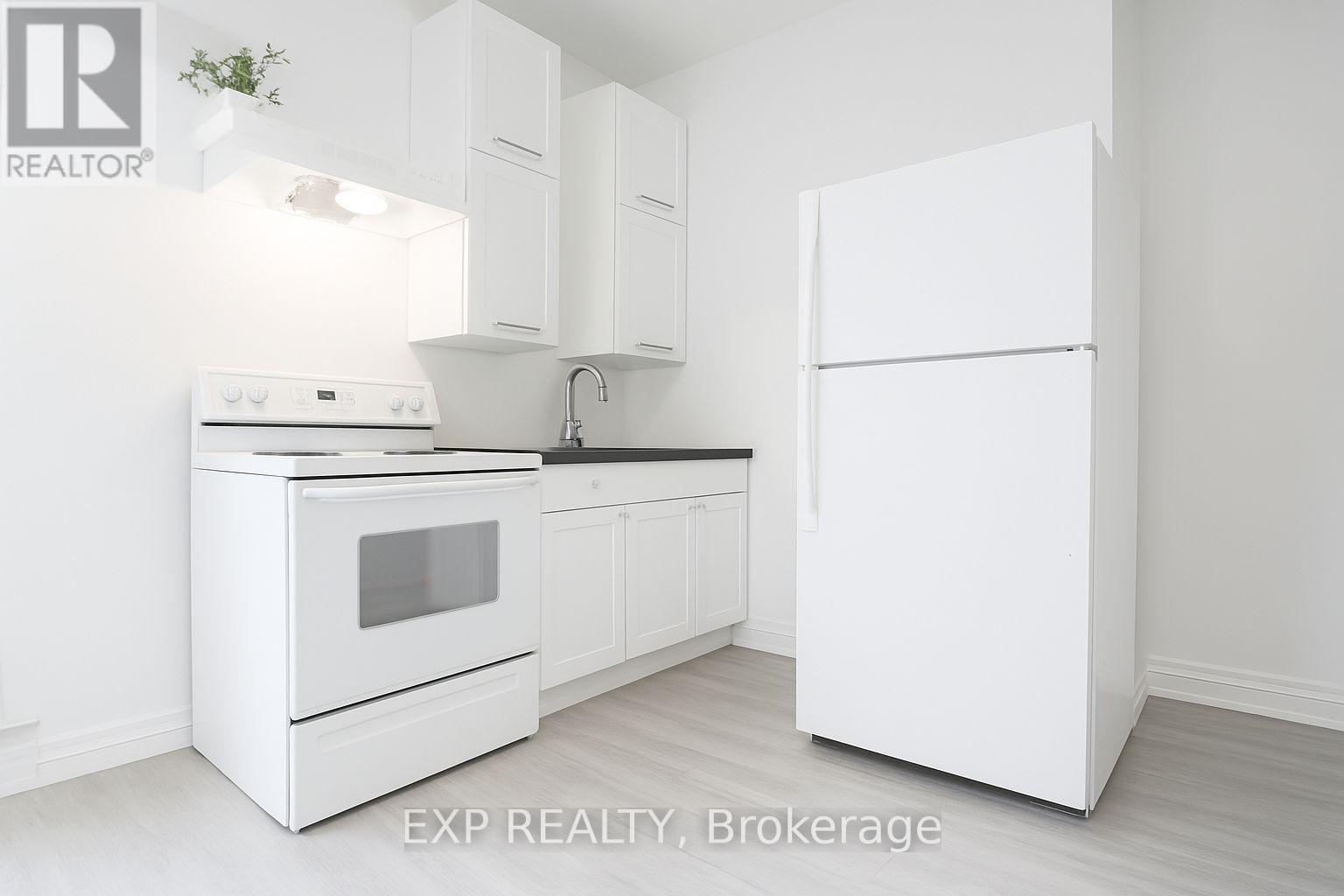 A white kitchen with a refrigerator, oven, and sink.