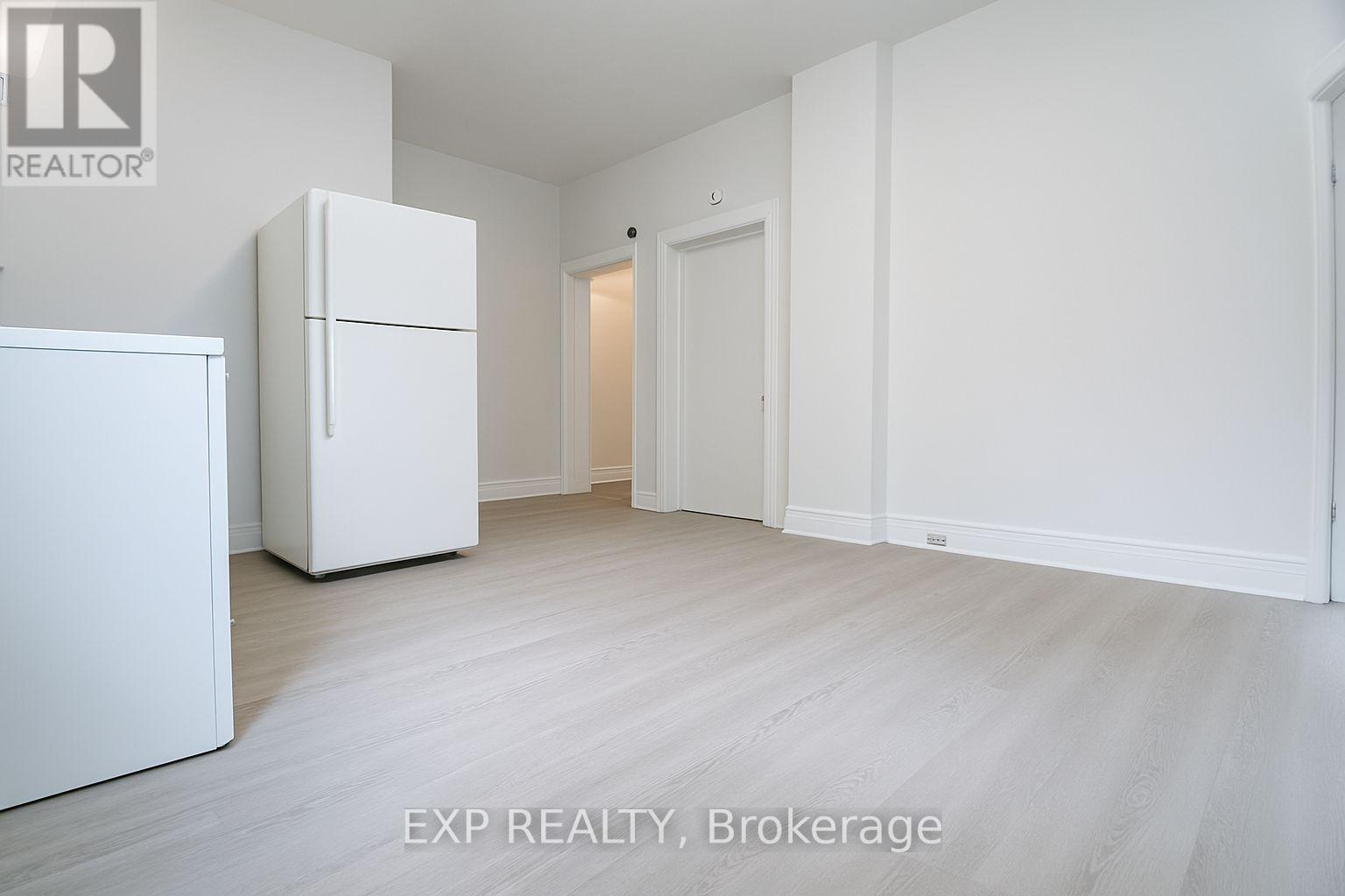 A white refrigerator is in a white room with a white door.