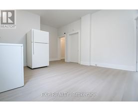 A white refrigerator is in a white room with a white door.