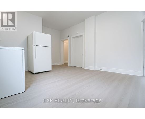 A white refrigerator is in a white room with a white door.