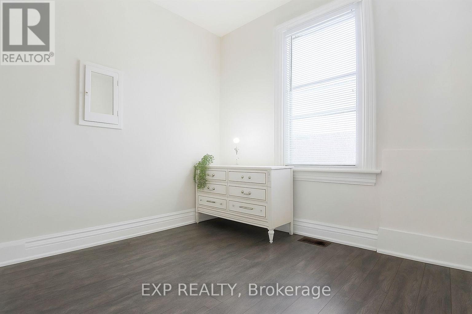 A white dresser with a mirror and a potted plant sits in a room with a window.