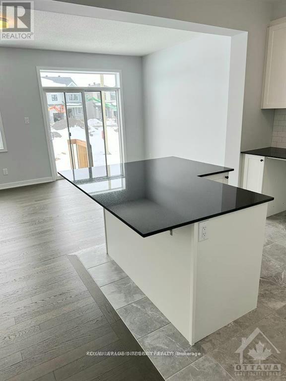 A black countertop in a white kitchen with a view of the outside.