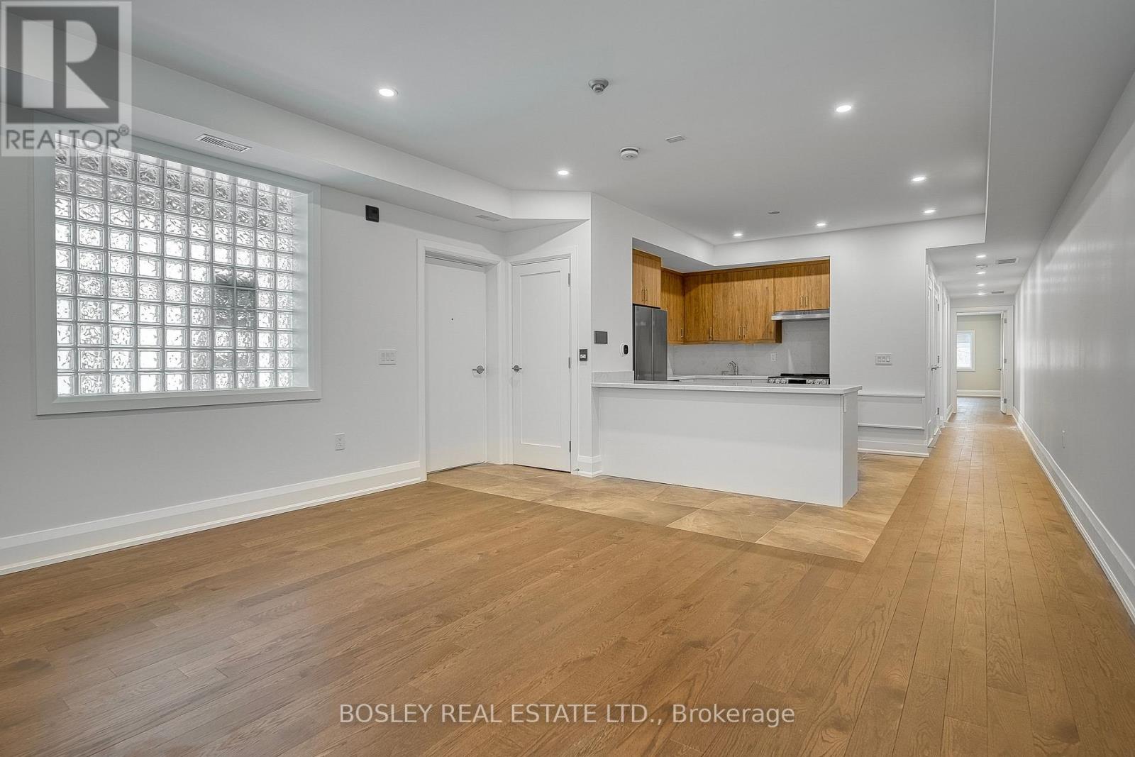 A spacious room with wooden flooring and a kitchen area in the background.