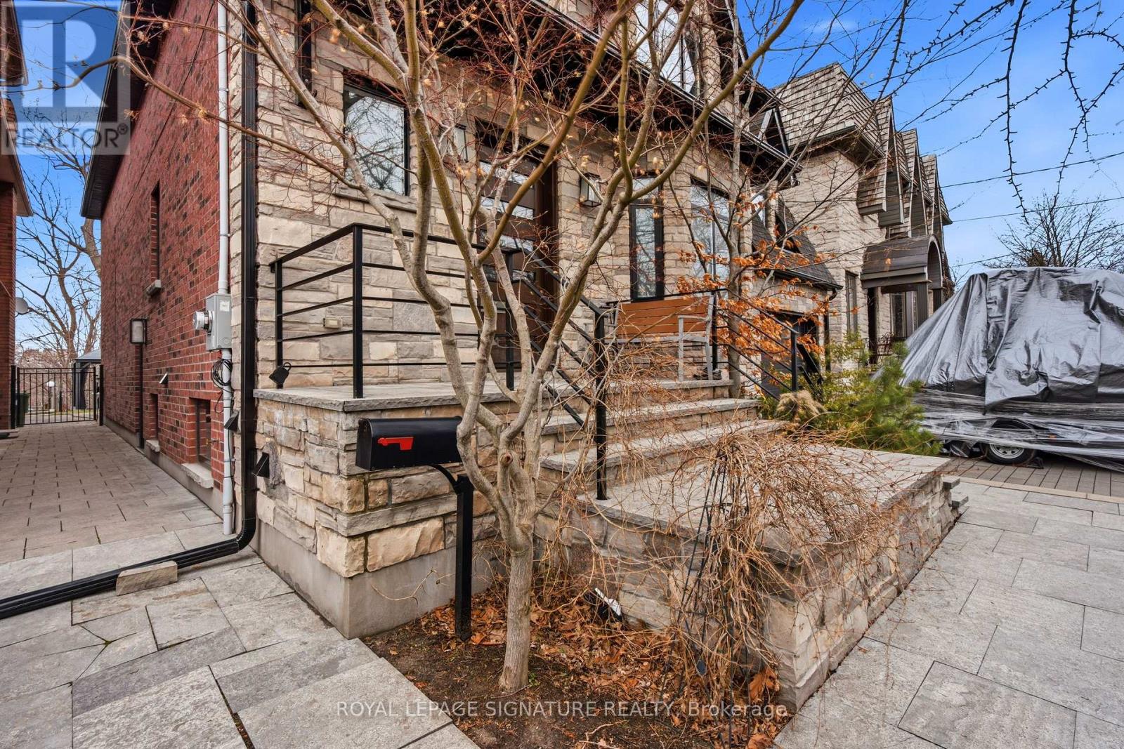 A tree in front of a house with a mailbox on the side.