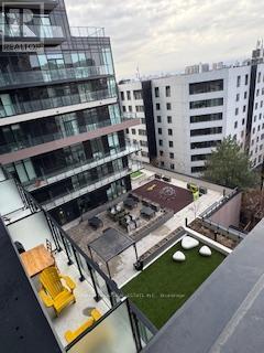 A modern building with a glass balcony overlooking a courtyard with a table and chairs.