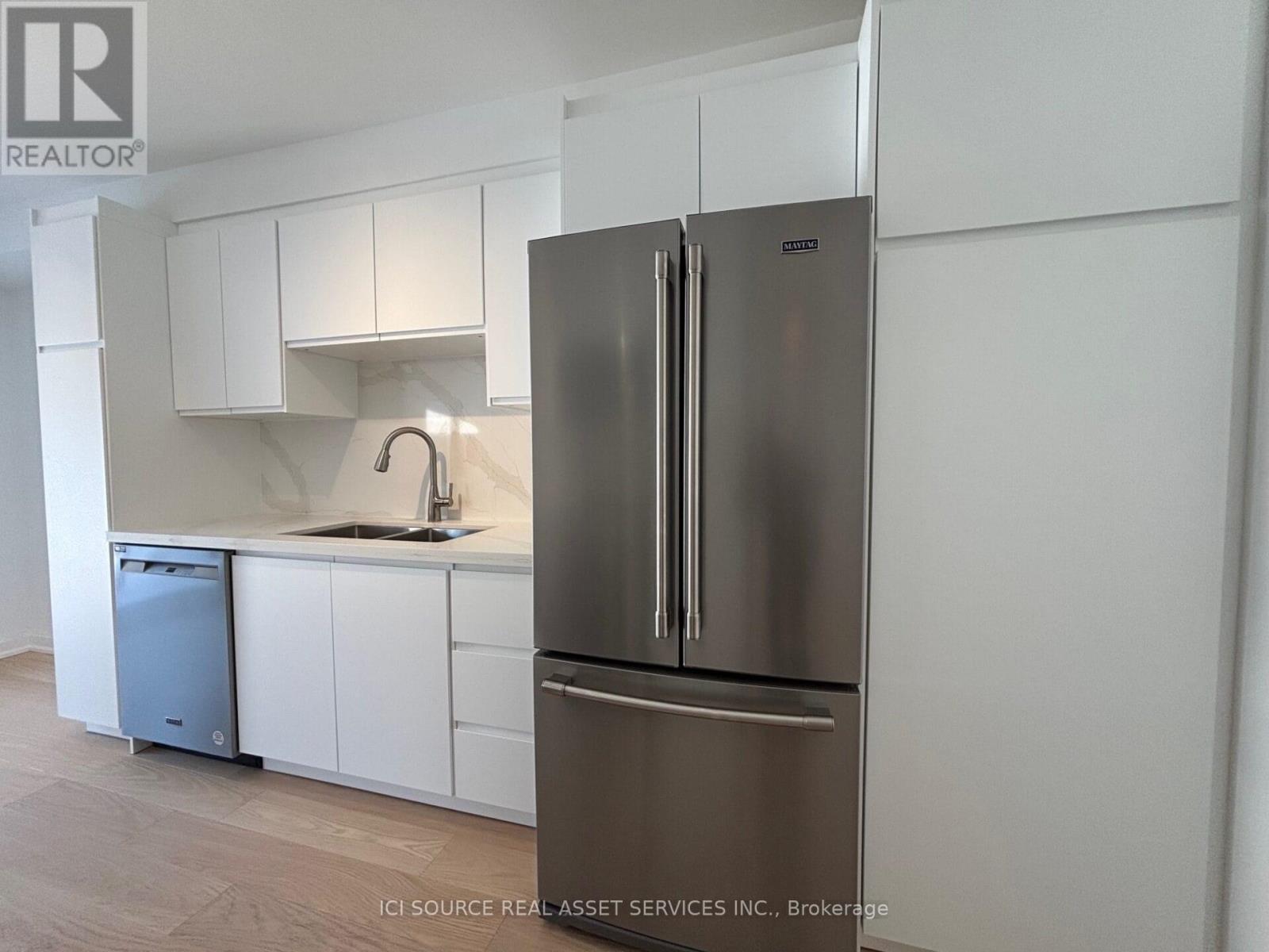 A stainless steel refrigerator stands in a kitchen with white cabinets.