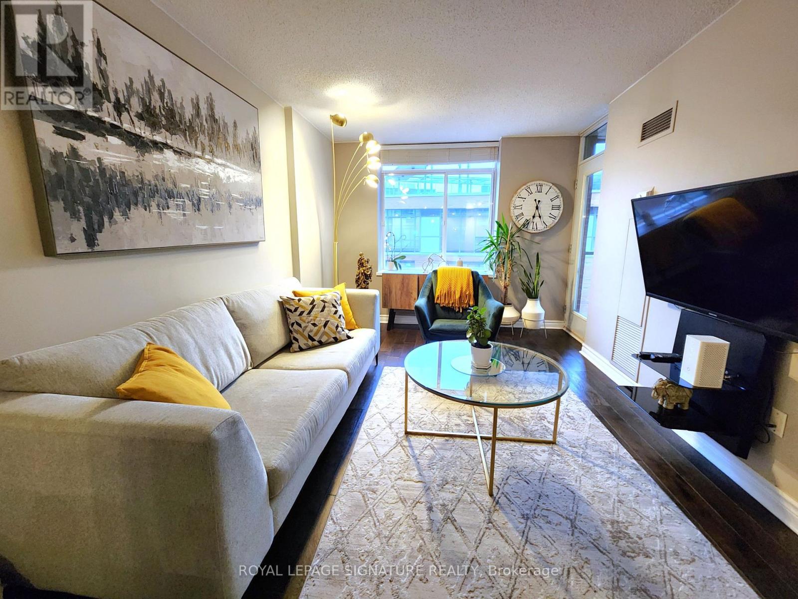 A living room with a grey couch, a glass coffee table, and a painting on the wall.