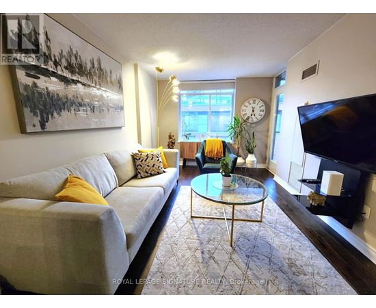 A living room with a grey couch, a glass coffee table, and a painting on the wall.
