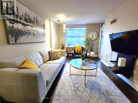 A living room with a grey couch, a glass coffee table, and a painting on the wall.