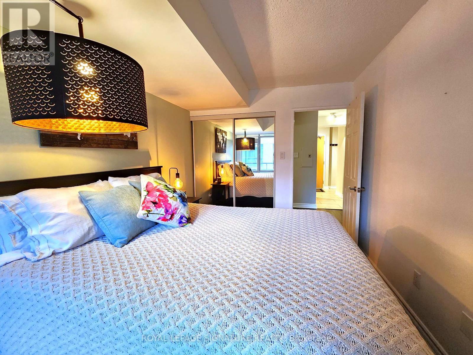 A bedroom with a large bed and a hanging light fixture.