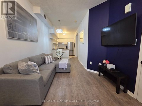 A living room with a grey couch and a black television mounted on the wall.
