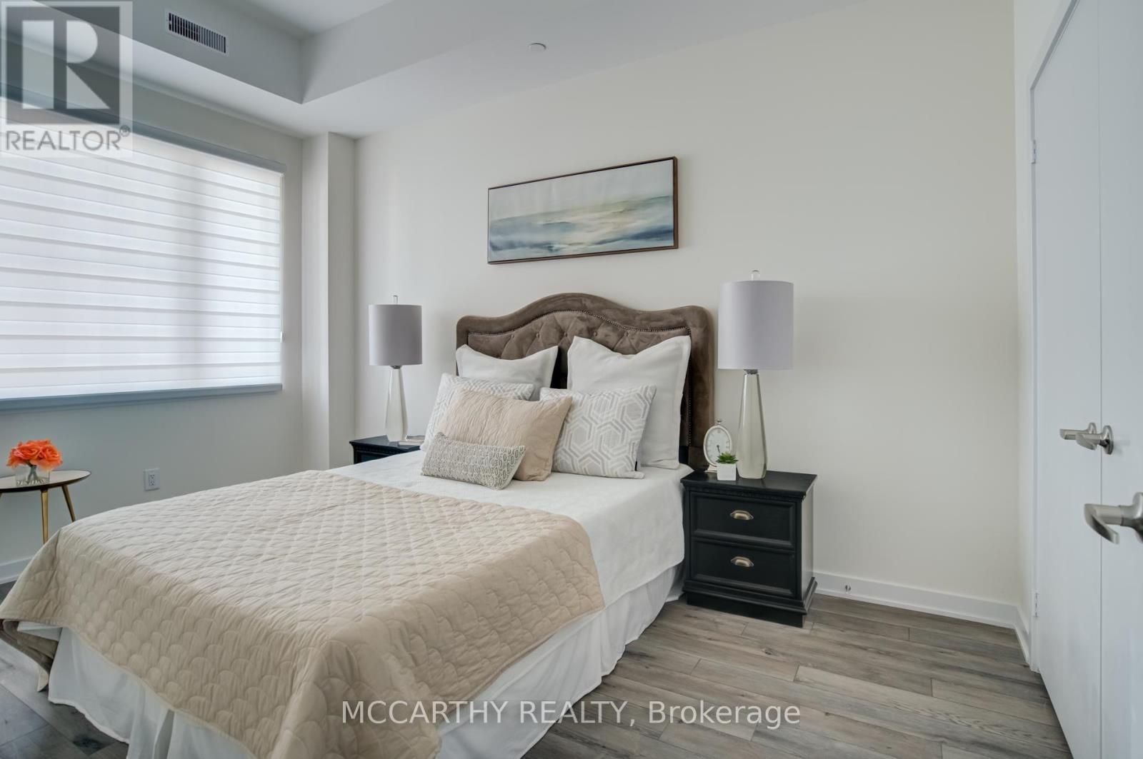 A bedroom with a large bed, a nightstand with a lamp, and a painting on the wall.