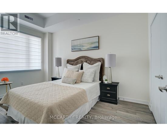 A bedroom with a large bed, a nightstand with a lamp, and a painting on the wall.