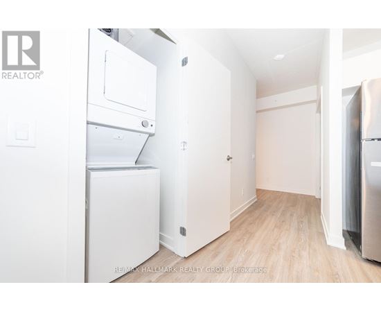 A white refrigerator is in a kitchen with wood floors and white walls.