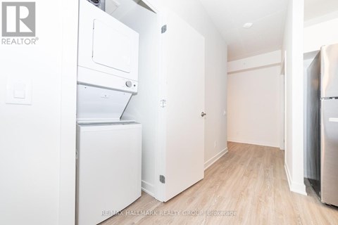 A white refrigerator is in a kitchen with wood floors and white walls.