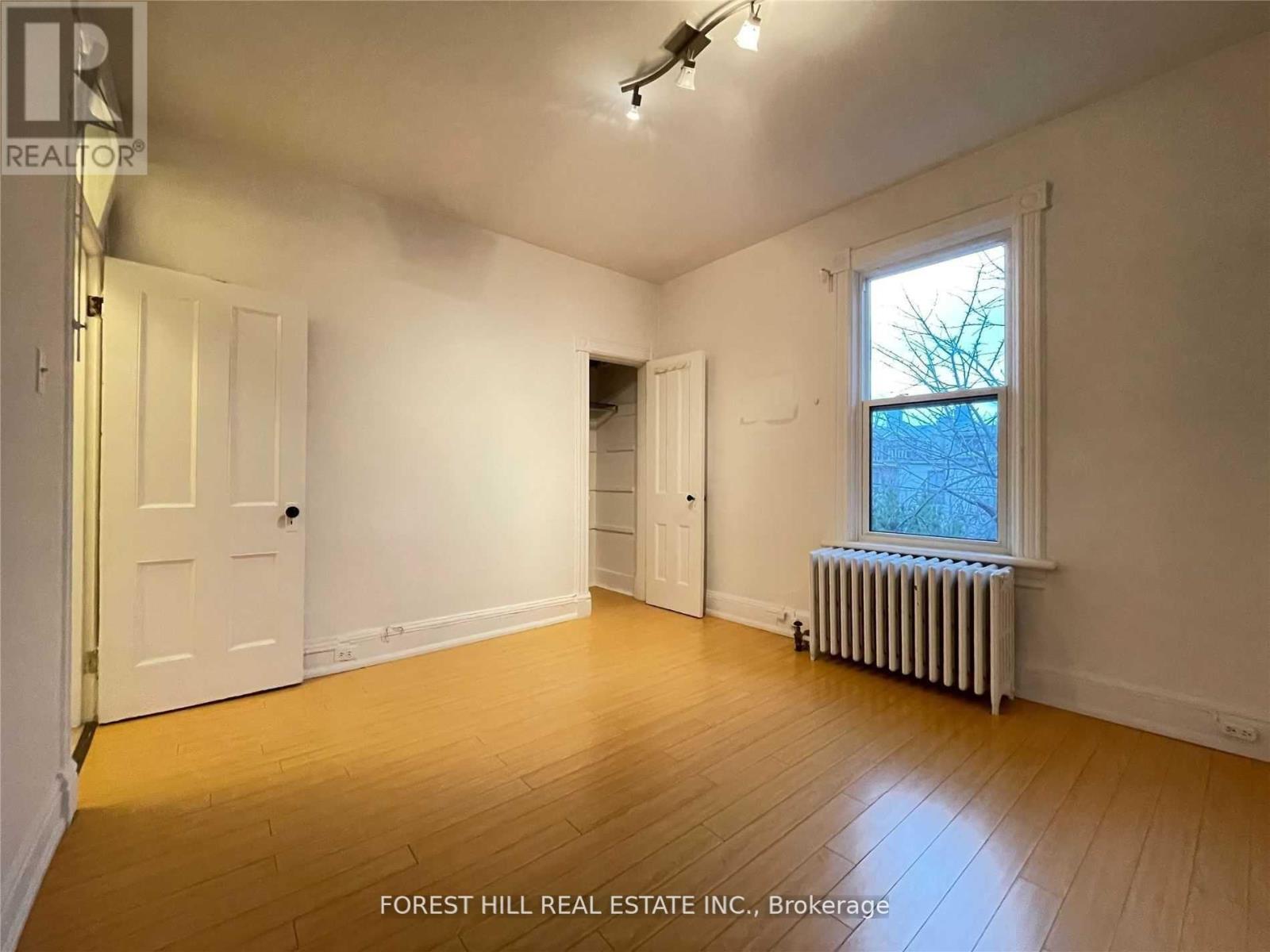 A room with wooden floors and white walls, with a window showing a tree outside.